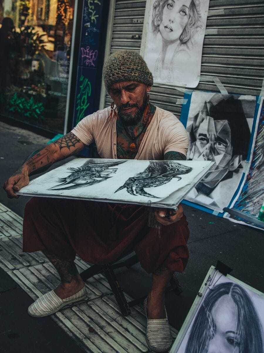 a man sitting on a sidewalk holding a piece of art