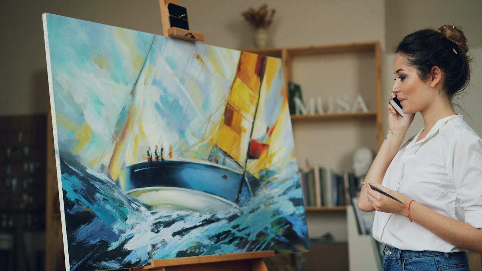 An artist talks on the phone near a painting.